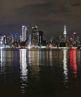 Night view of the New York City skyline with illuminated buildings reflecting on the water. - Olive Oil Times