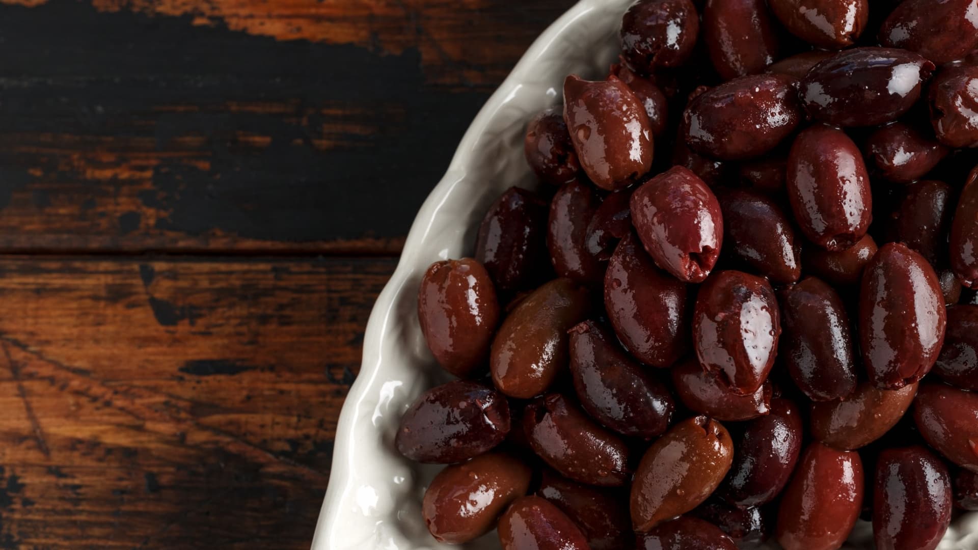 A close-up view of a bowl filled with various types of olives, showcasing their dark and light hues. - Olive Oil Times