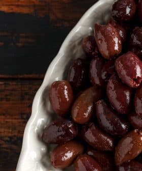 A close-up view of a bowl filled with various types of olives, showcasing their dark and light hues. - Olive Oil Times