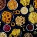 An assortment of snack foods including chips, pretzels, and popcorn arranged in bowls on a dark surface. - Olive Oil Times
