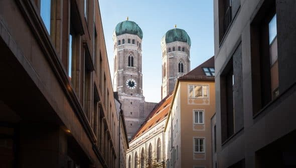 View of the twin towers of Munich's Cathedral framed by surrounding buildings. - Olive Oil Times