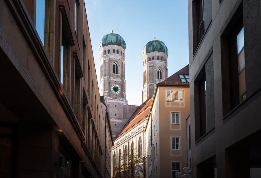 View of the twin towers of Munich's Cathedral framed by surrounding buildings. - Olive Oil Times