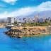 Coastal view featuring a city skyline with mountains in the background and clear blue water. - Olive Oil Times