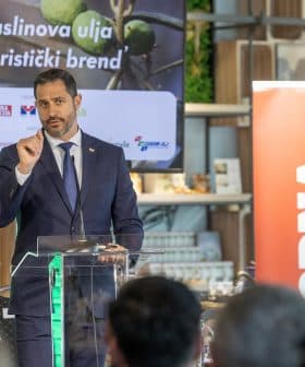 A man in a suit speaking at a podium during an event about olive oil as a tourist brand. - Olive Oil Times