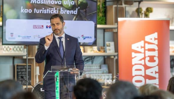 A man in a suit speaking at a podium during an event about olive oil as a tourist brand. - Olive Oil Times