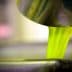 Bright green olive oil pouring from a metal container into a bowl. - Olive Oil Times