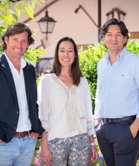 Three individuals standing outdoors, smiling and posing for the camera in a garden setting. - Olive Oil Times