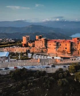 Aerial view of a historic castle surrounded by mountains and greenery. - Olive Oil Times