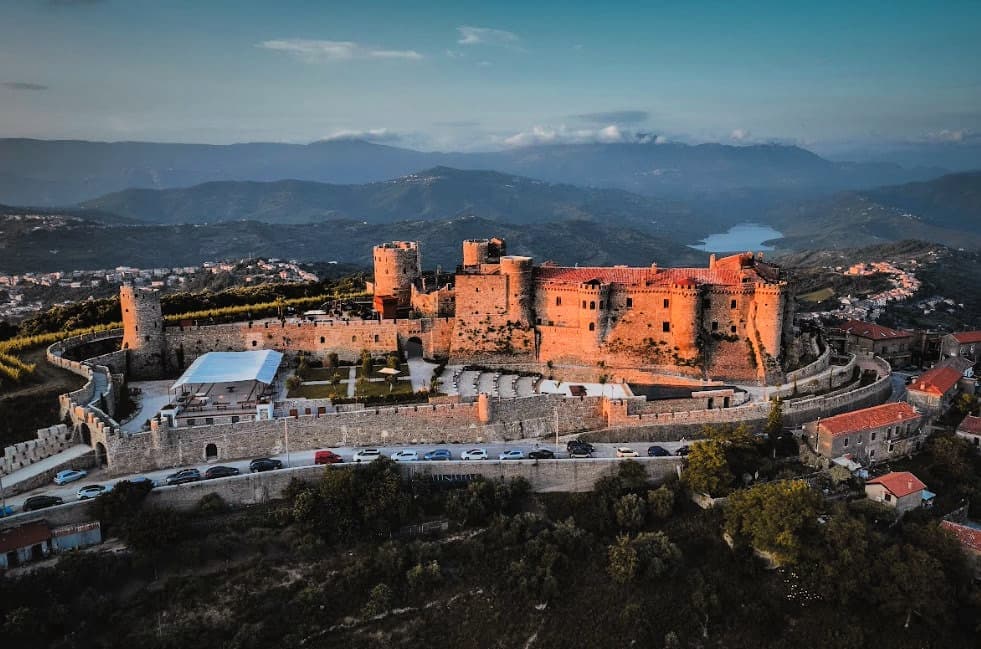Aerial view of a historic castle surrounded by mountains and greenery. - Olive Oil Times