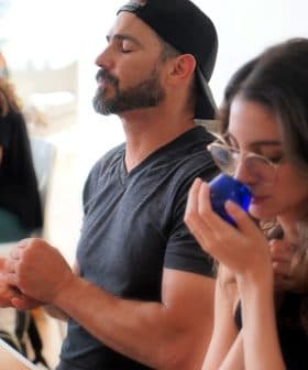 Two participants in a tasting session, one smelling from a blue container while the other is seated with eyes closed. - Olive Oil Times