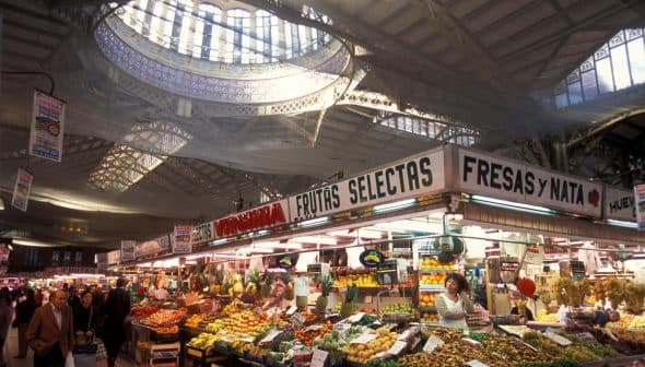 Market stall displaying a variety of fruits and vegetables under a large skylight. - Olive Oil Times