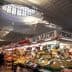 Market stall displaying a variety of fruits and vegetables under a large skylight. - Olive Oil Times