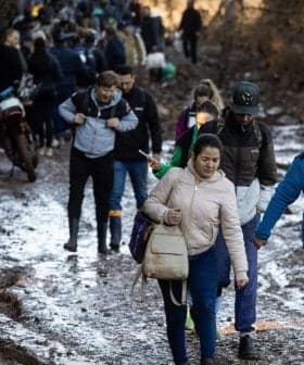 A group of people walking along a muddy path in a wooded area, some carrying bags. - Olive Oil Times