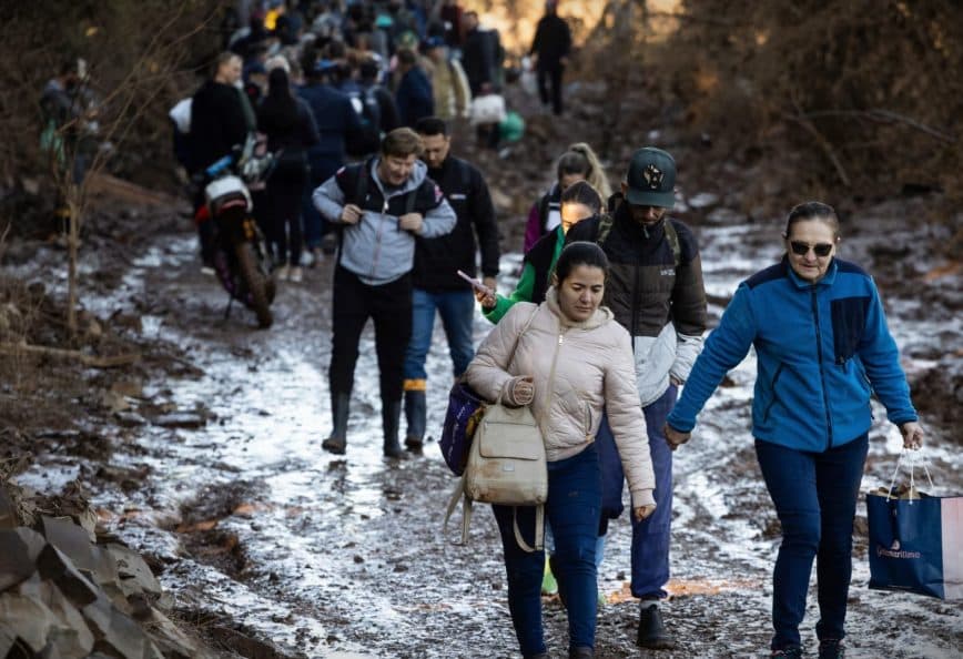 A group of people walking along a muddy path in a wooded area, some carrying bags. - Olive Oil Times