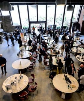 Interior of a spacious event venue featuring round tables and attendees engaged in conversation. - Olive Oil Times