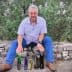 A man seated on a stone wall with various olive oil bottles displayed in front of him. - Olive Oil Times