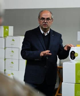 A man in a suit presenting a container of olive oil in a warehouse setting. - Olive Oil Times