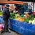 Man examining fresh vegetables at a market stall with various produce displayed. - Olive Oil Times