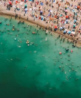 Aerial view of a crowded beach with swimmers and colorful umbrellas along the shoreline. - Olive Oil Times