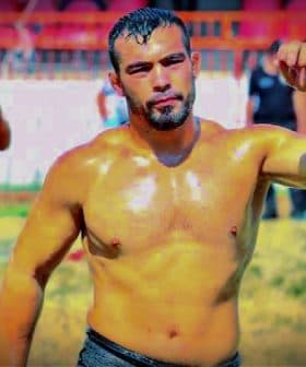 A male wrestler with a muscular build, wearing traditional oil wrestling attire, standing in a field. - Olive Oil Times
