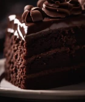 Slice of chocolate layer cake with chocolate frosting and decorative swirls on top. - Olive Oil Times