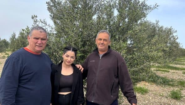Three individuals standing together in front of an olive tree in an outdoor setting. - Olive Oil Times