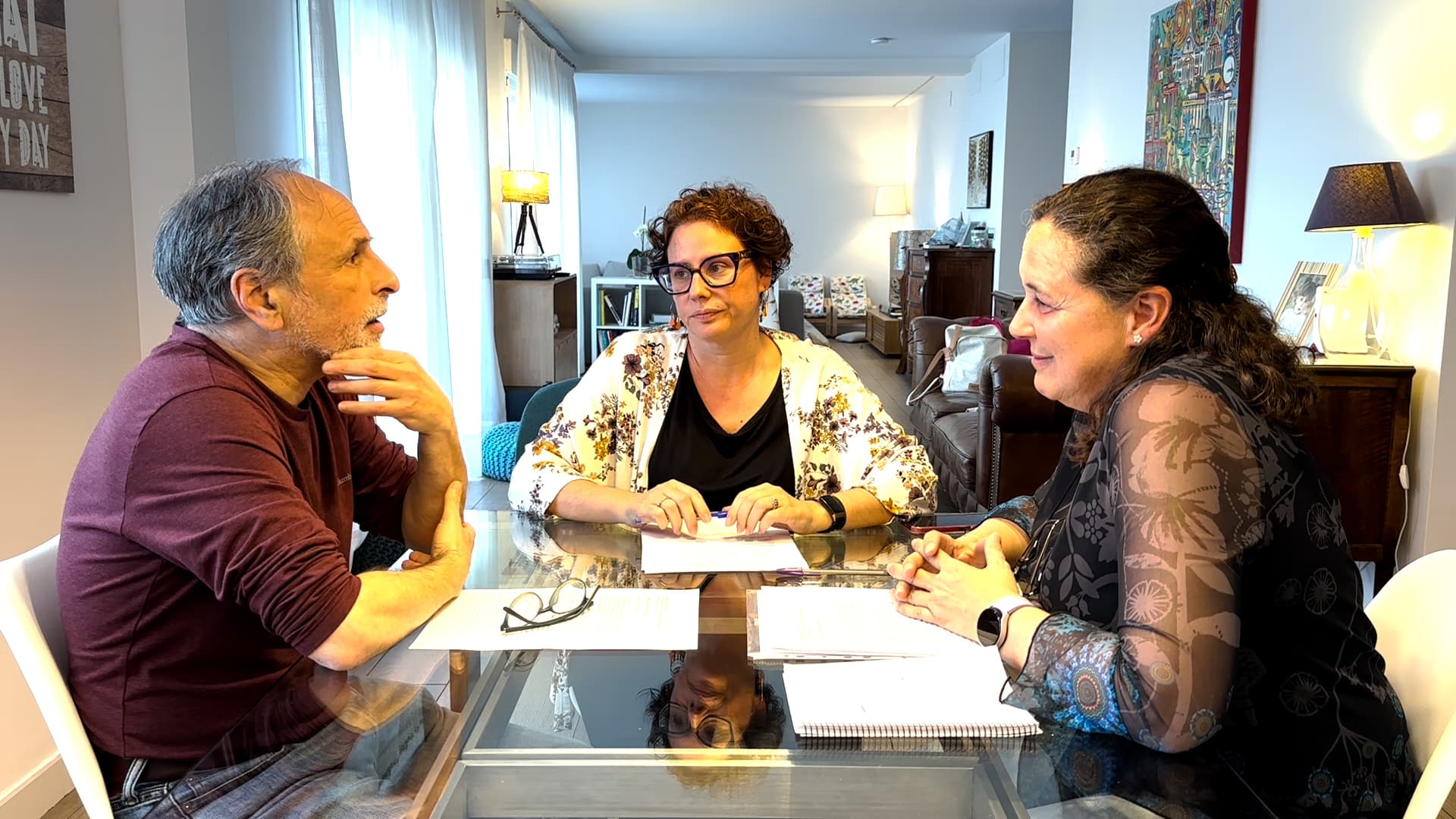 Three individuals seated at a table engaged in a discussion with papers in front of them. - Olive Oil Times