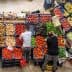 Two individuals arranging fresh vegetables and fruits at a market stall with various produce. - Olive Oil Times