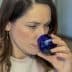 Woman with brown hair holding a blue tasting glass labeled 'Olive Oil' close to her face. - Olive Oil Times
