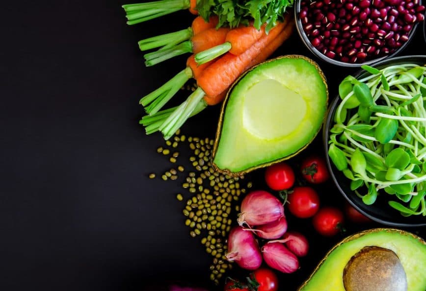 An assortment of fresh vegetables including carrots, celery, and avocado arranged on a dark surface. - Olive Oil Times