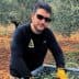Man wearing sunglasses and gloves sorting olive leaves in a container in an olive grove. - Olive Oil Times