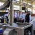 Group of individuals observing an oil extraction machine during a demonstration in a factory setting. - Olive Oil Times