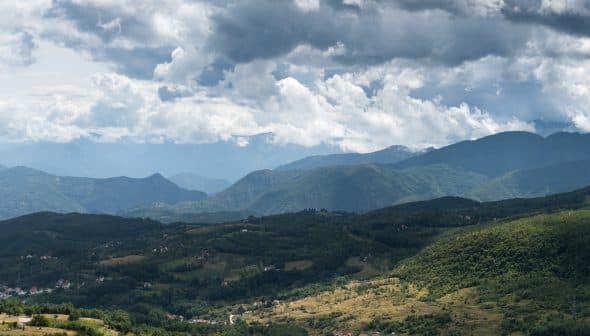A panoramic view of mountains under a cloudy sky with varying shades of green vegetation. - Olive Oil Times