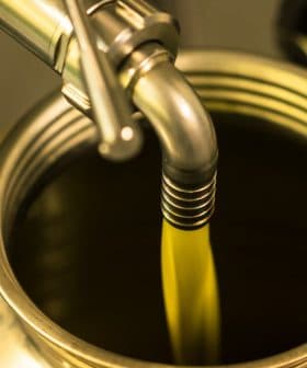Olive oil being poured from a metal canister into a container. - Olive Oil Times