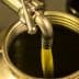 Olive oil being poured from a metal canister into a container. - Olive Oil Times