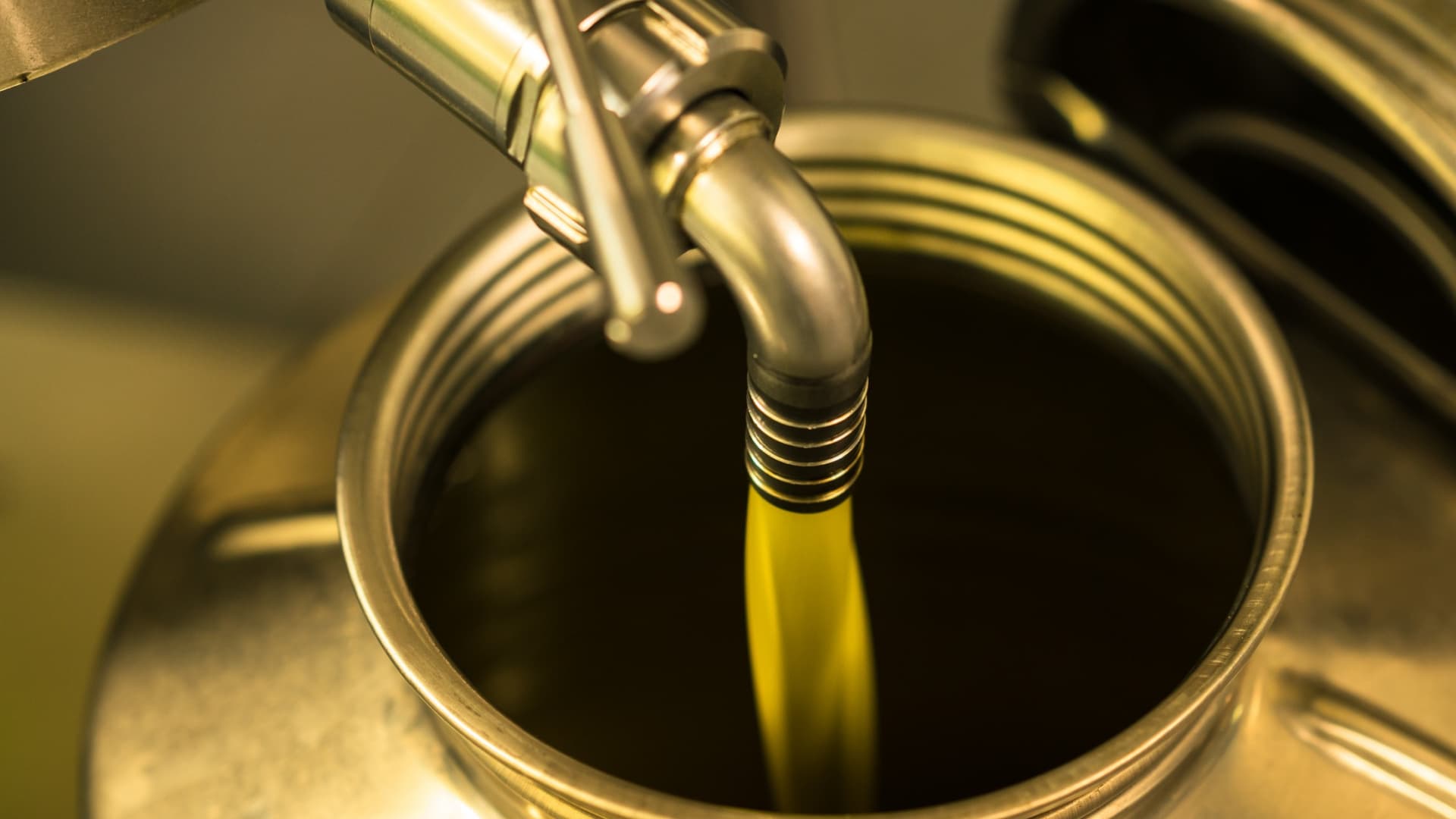 Olive oil being poured from a metal canister into a container. - Olive Oil Times