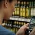 A woman photographing olive oil bottles on a shelf using a smartphone in a store. - Olive Oil Times