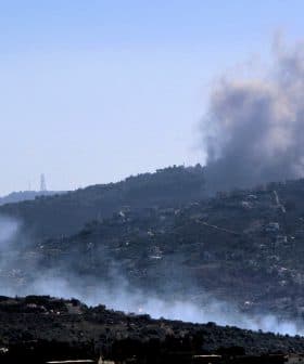 Smoke billowing from a mountainous region with a clear blue sky in the background. - Olive Oil Times