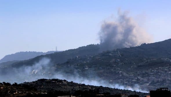 Smoke billowing from a mountainous region with a clear blue sky in the background. - Olive Oil Times