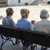 Three elderly men sitting on a bench, viewed from behind, in a public square. - Olive Oil Times