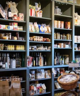 Wooden shelves filled with jars, bottles, and packaged food items in a grocery store. - Olive Oil Times