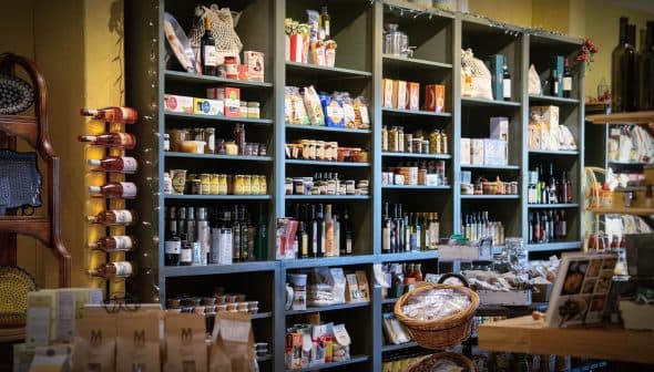Wooden shelves filled with jars, bottles, and packaged food items in a grocery store. - Olive Oil Times