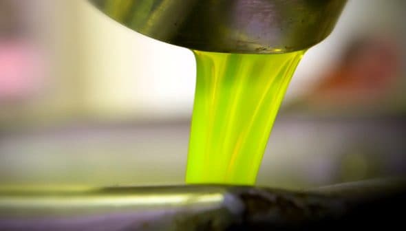 Bright green olive oil pouring from a metal container into a bowl. - Olive Oil Times