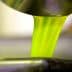 Bright green olive oil pouring from a metal container into a bowl. - Olive Oil Times