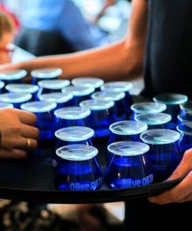 A tray holding multiple blue glasses filled with olive oil being served at an event. - Olive Oil Times