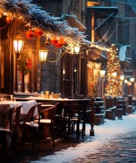Outdoor dining area with tables and chairs on a snowy street during winter evening. - Olive Oil Times