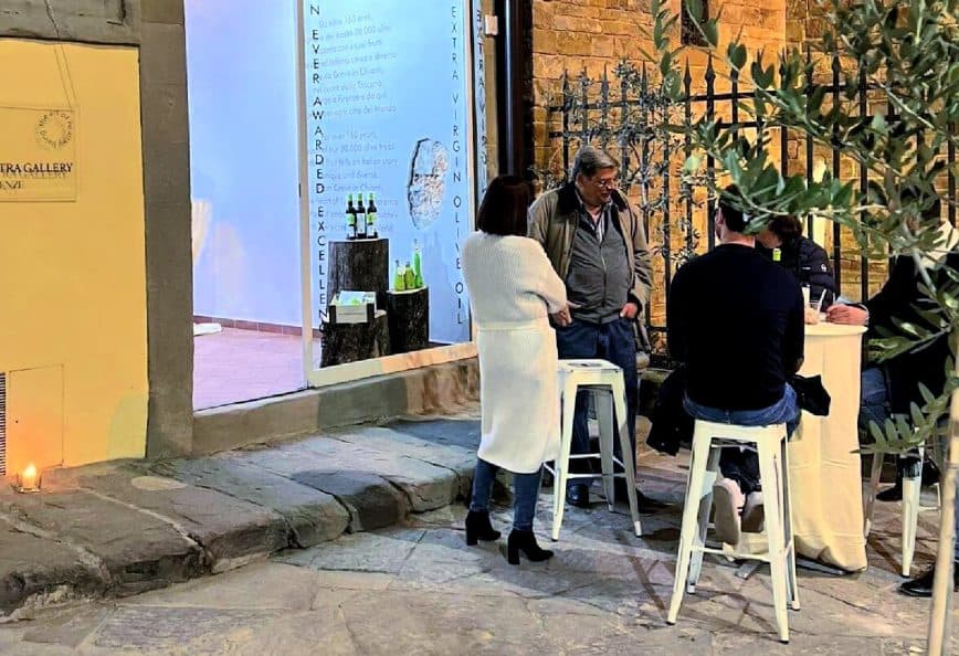 A group of four people gathered around a table outside an art gallery, engaged in conversation. - Olive Oil Times