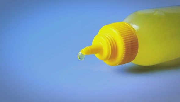 Yellow plastic mustard bottle with a yellow cap and a small drop of mustard at the tip. - Olive Oil Times