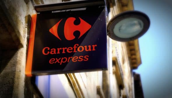 Sign for Carrefour Express featuring a red logo and the name in orange text on a black background. - Olive Oil Times
