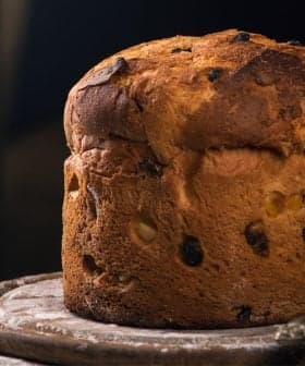 A round loaf of bread with a golden-brown crust and visible raisins on a wooden surface. - Olive Oil Times